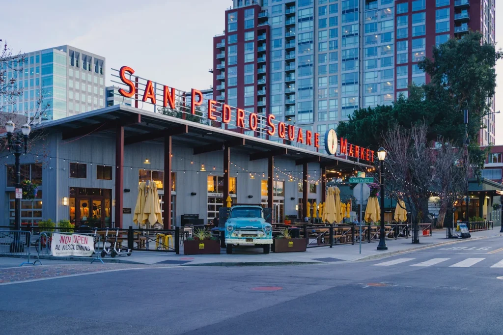 San Pedro Square Market with patio seating, a vintage blue truck, and downtown towers behind it