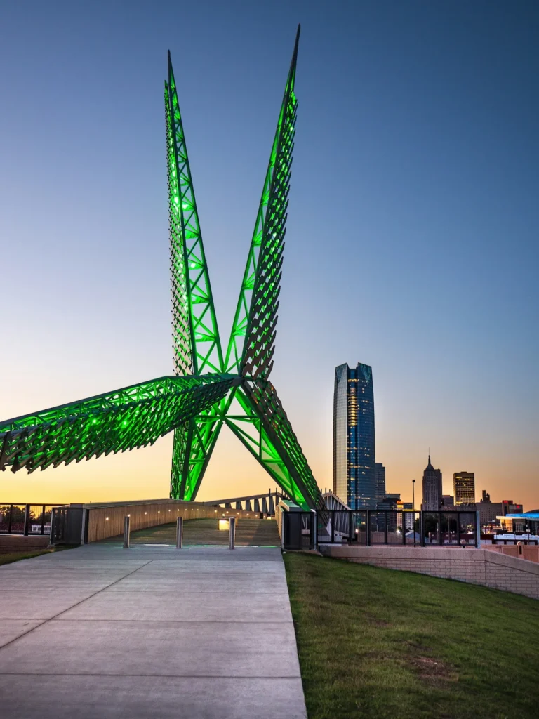 The green lit Skydance Bridge structure with the Oklahoma City skyline in the background