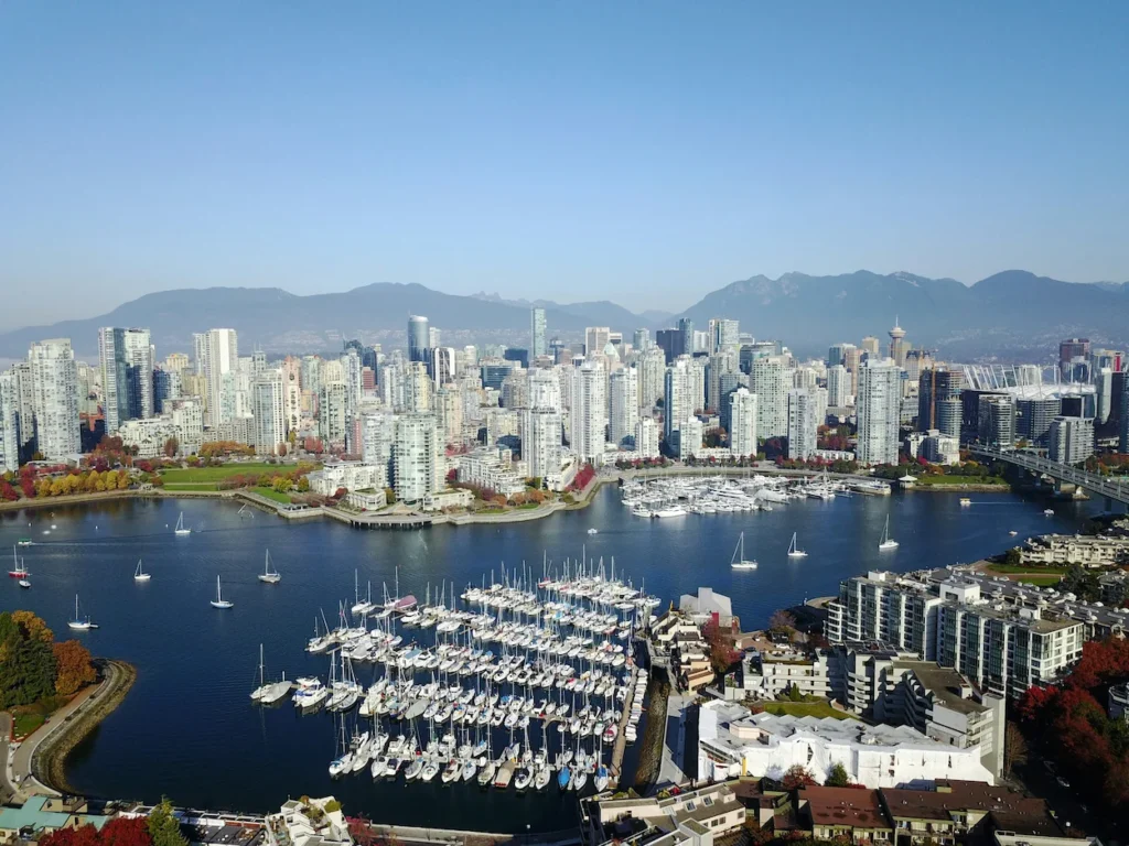 An aerial view of the downtown Vancouver skyline, a bustling marina, and mountains in the background