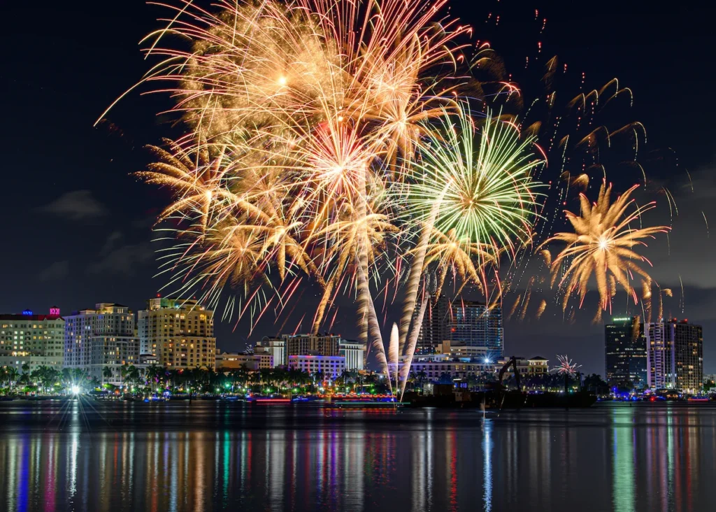 Vibrant gold and green fireworks bursting over the illuminated downtown skyline in West Palm Beach, Florida
