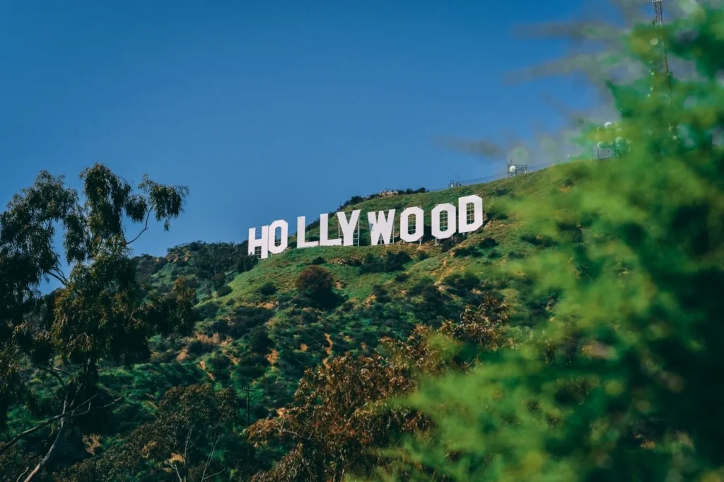 The iconic white Hollywood Sign on a grassy green hillside under a clear blue sky