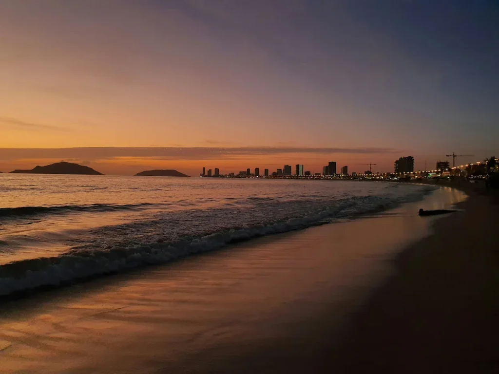 A sunset view over the ocean beach with the distant Mazatlán skyline