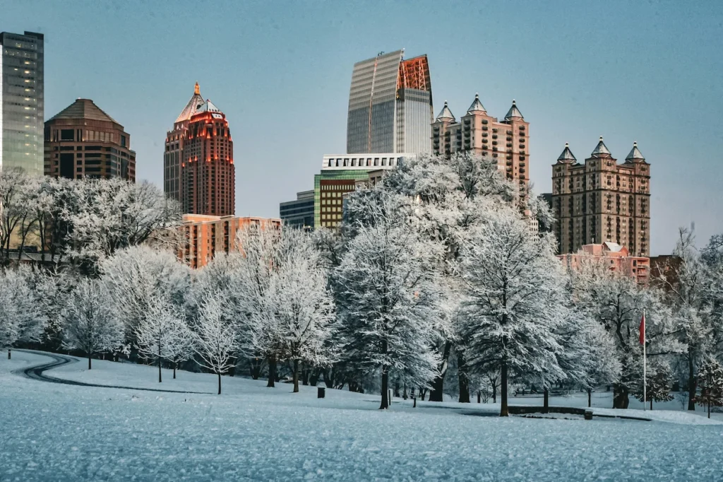 Snow-covered trees and lawns in Piedmont Park with the Atlanta skyline in the background