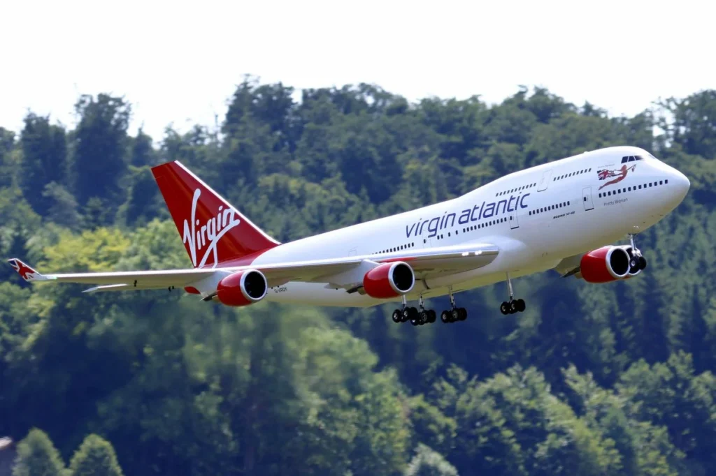 Virgin Atlantic Boeing 747 aircraft climbing with a green forest background