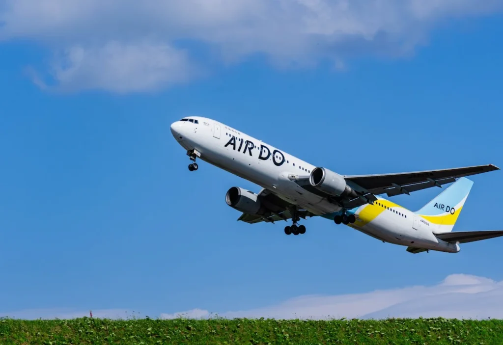 Air Do Boeing 767 climbing after takeoff over a grassy hill