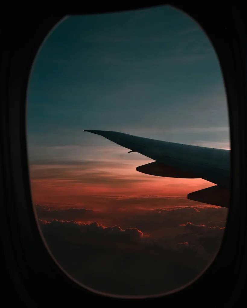 View from an airplane window looking out at a wing over sunset clouds