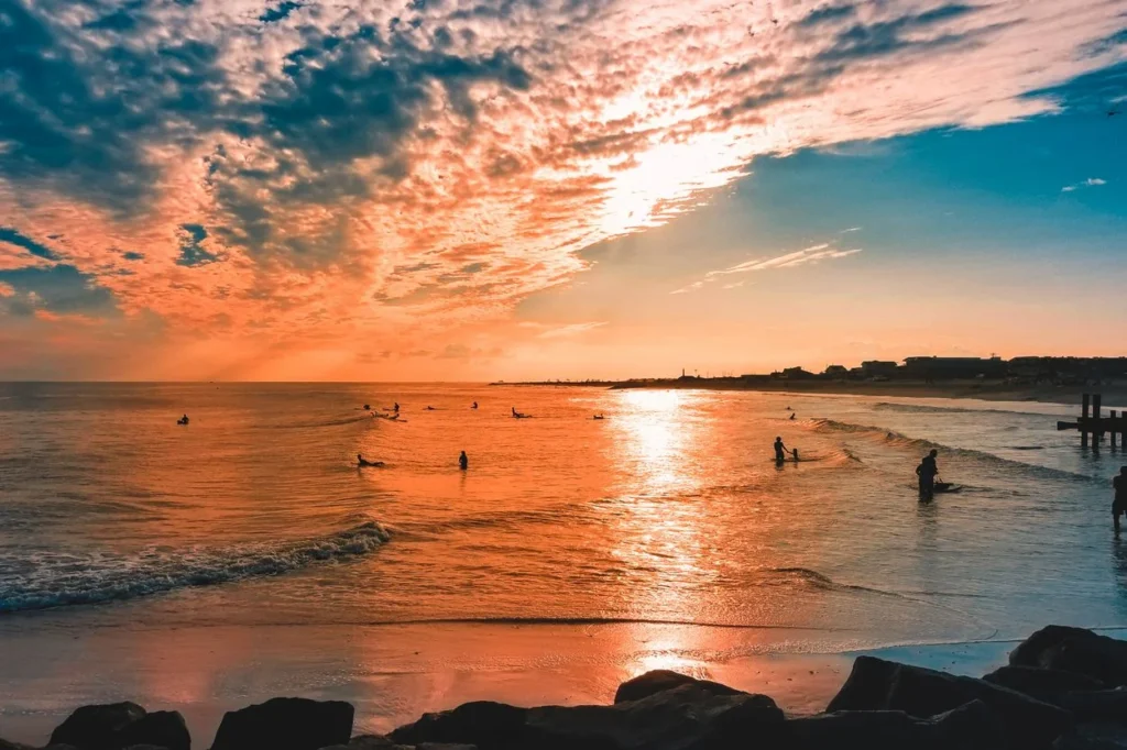 Silhouetted surfers waiting in the ocean during a vibrant orange and pink sunrise over Cape May Beach