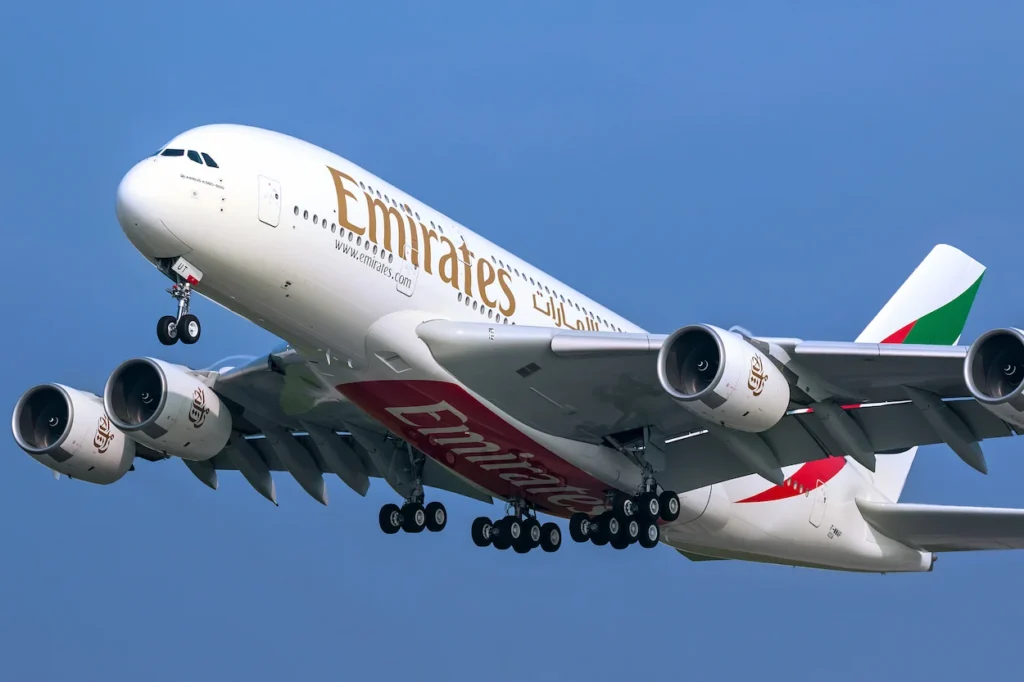 Emirates Airbus A380 passenger plane flying with landing gear visible against a blue sky