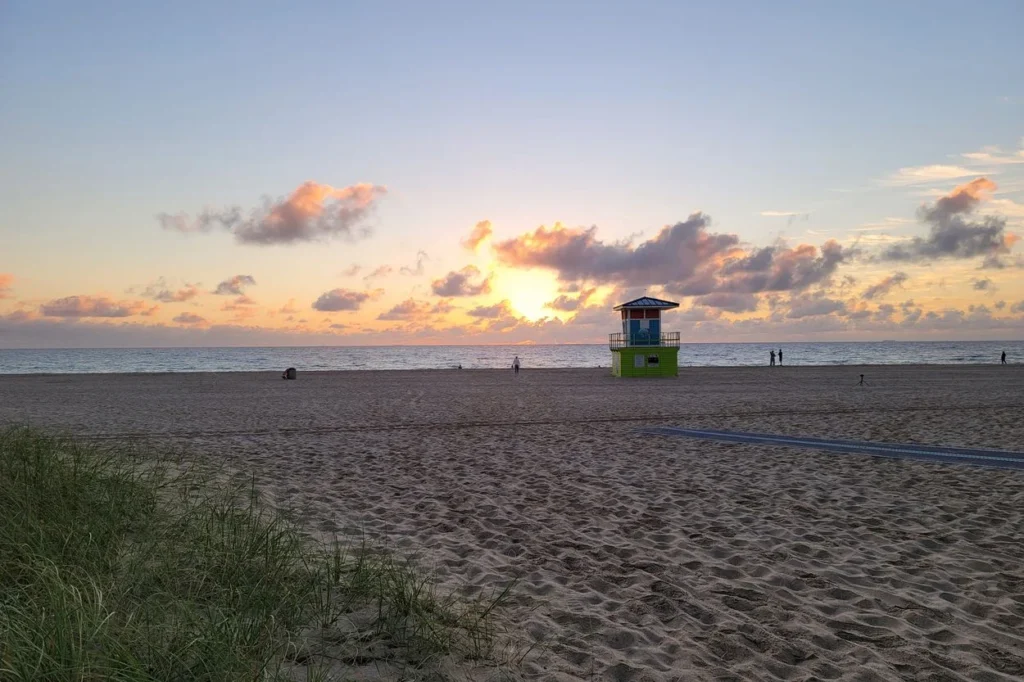 A colorful sunrise over Fort Lauderdale Beach featuring a bright green lifeguard tower on the sand