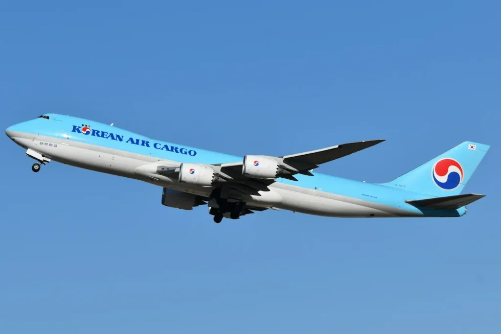 A light blue Korean Air Cargo Boeing 747-8F freighter aircraft climbing into a clear blue sky