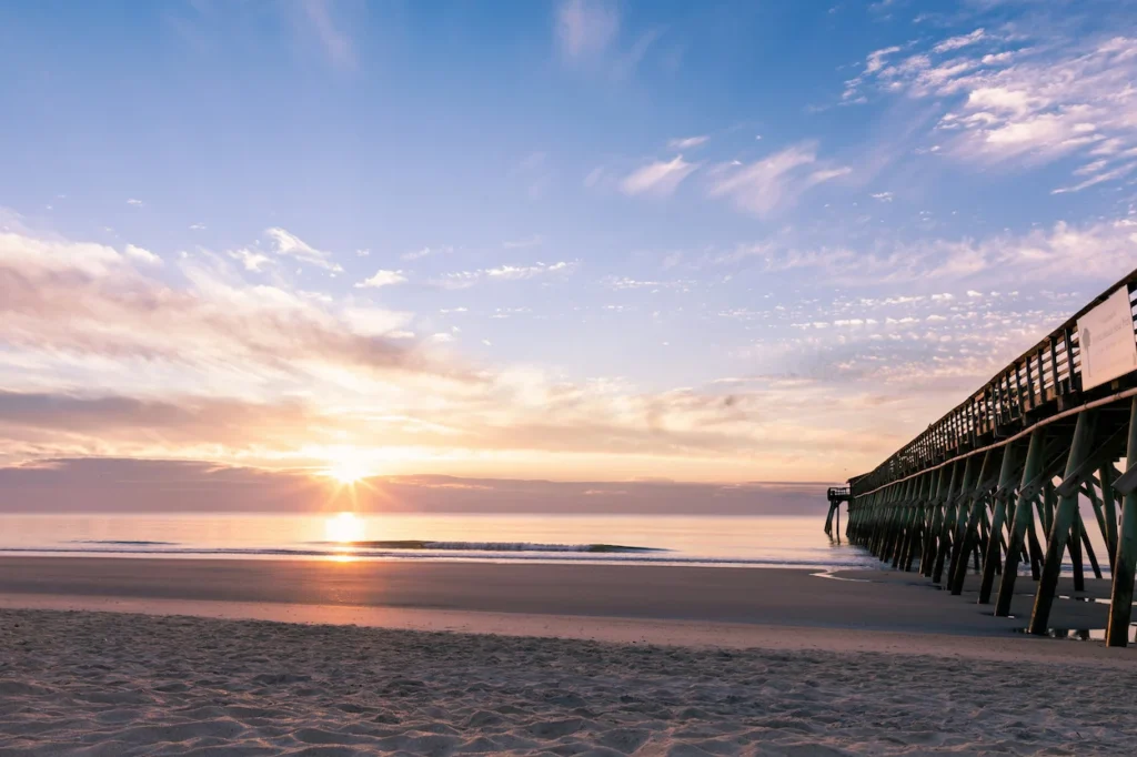 A golden sunrise over the ocean next to the wooden Myrtle Beach Pier jutting out into the water