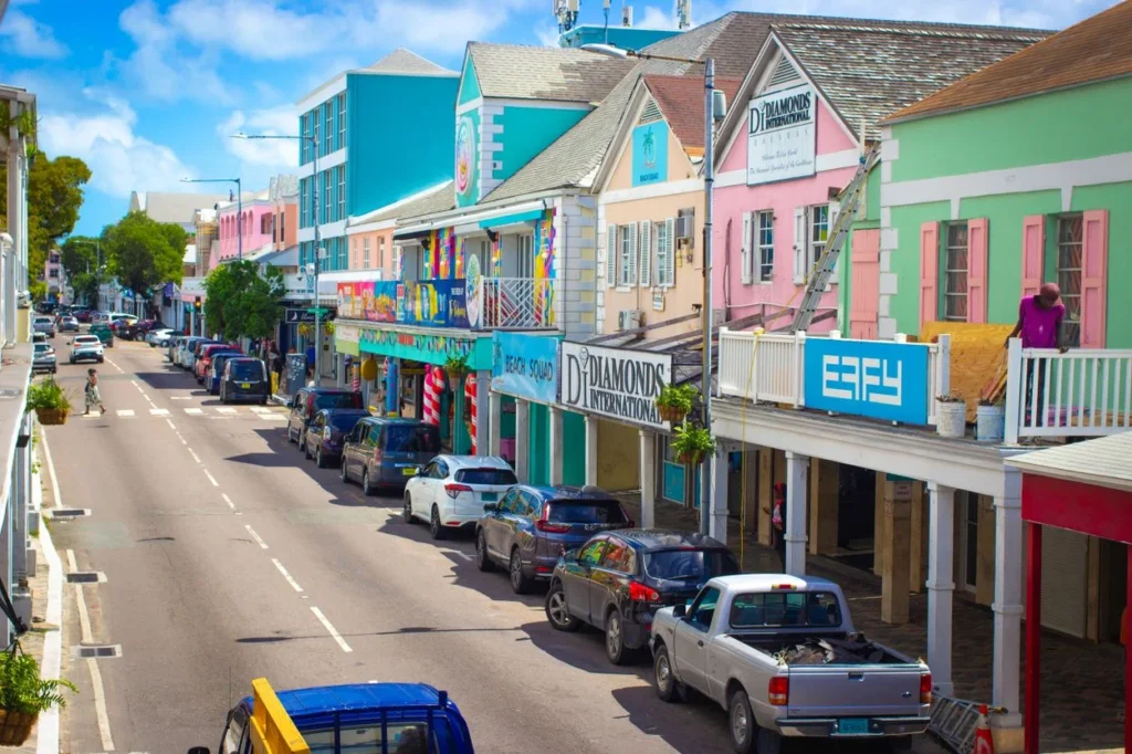 A row of colorful pastel shops and parked cars along a street in downtown Nassau, Bahamas