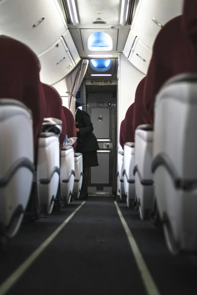 Qatar Airways airplane cabin aisle with burgundy seats and a cabin crew member