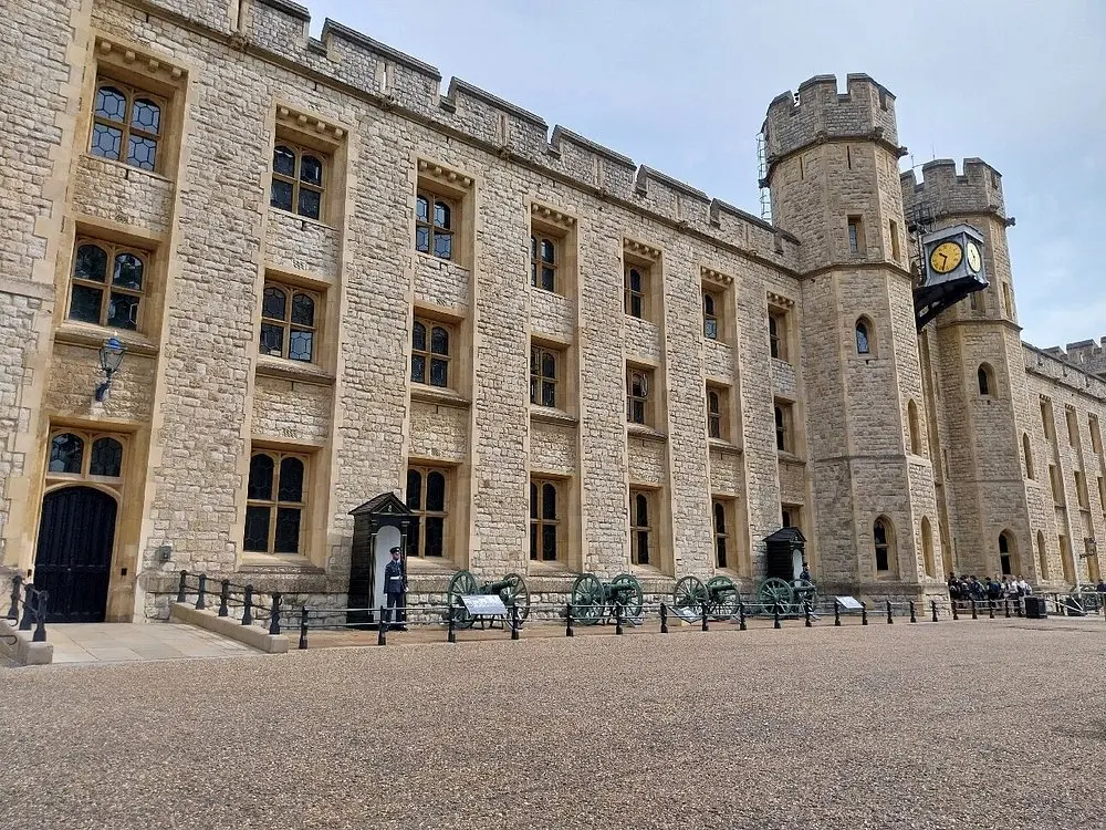 The stone fortress walls of the Tower of London with a guard standing outside.