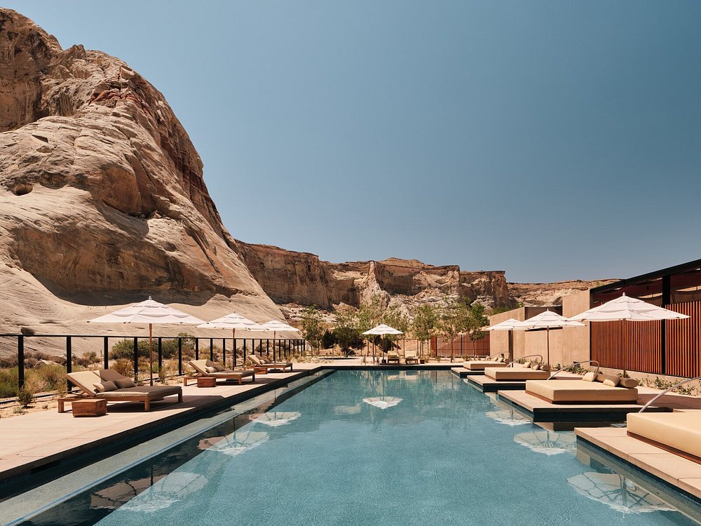 Amangiri resort pool with lounge chairs and umbrellas set against desert cliffs.