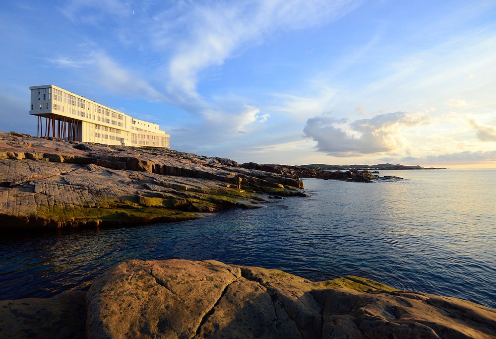 Fogo Island Inn perched on stilts above rocky coastline overlooking the ocean at sunset.
