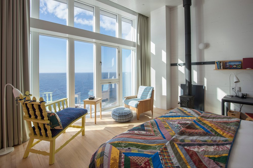 Fogo Island Inn room with colorful quilt, modern decor, and large windows overlooking the ocean.