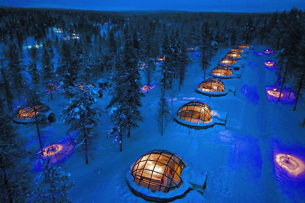 Kakslauttanen Arctic Resort glass igloos glowing at night in a snowy forest.
