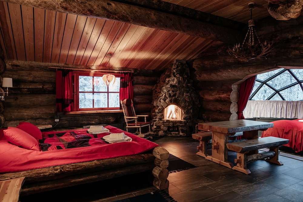 Kakslauttanen Arctic Resort log cabin room with red bedding, stone fireplace, and wooden furniture.