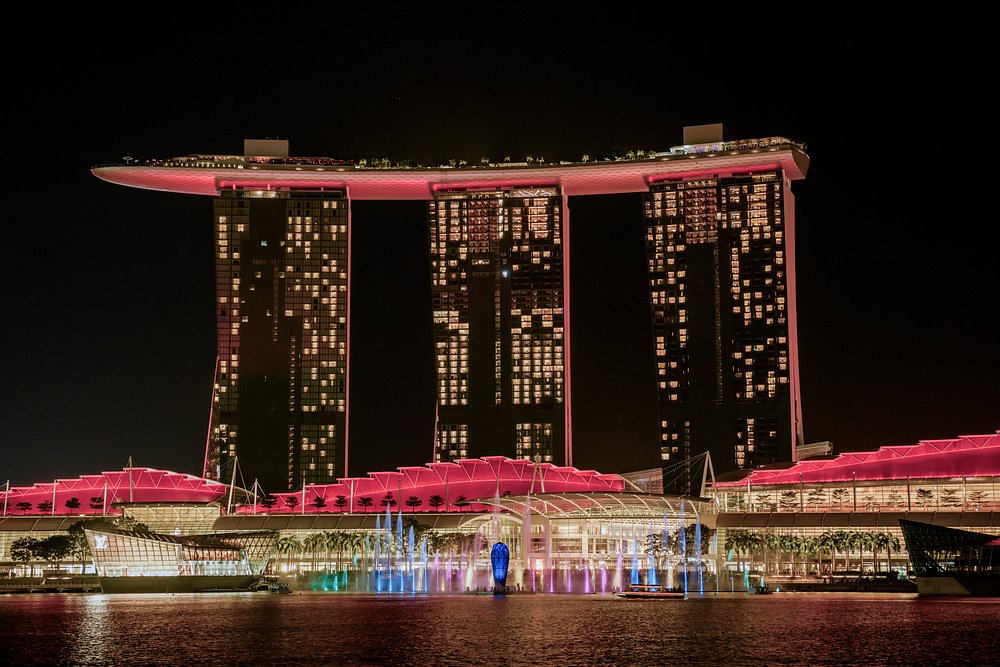 Marina Bay Sands in Singapore lit up at night with pink lights and water show.