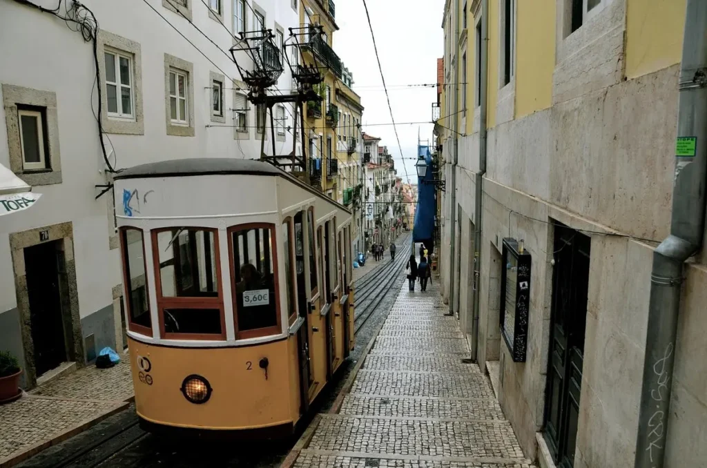 A yellow tram travels down a steep cobblestone street in Lisbon, Portugal.