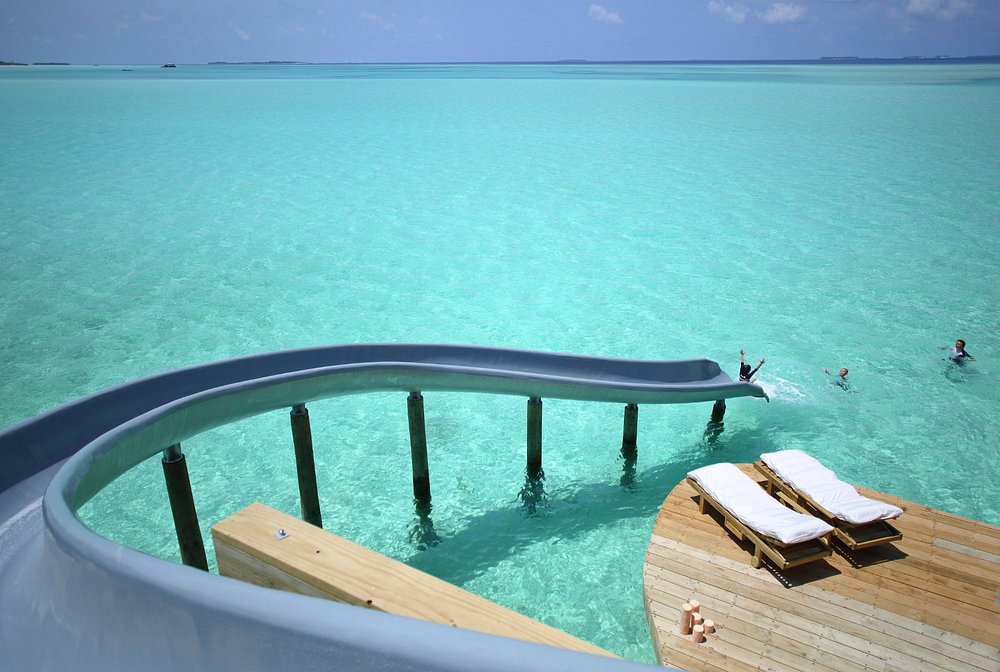 Soneva Jani resort with water slide leading into clear turquoise ocean beside sun loungers.