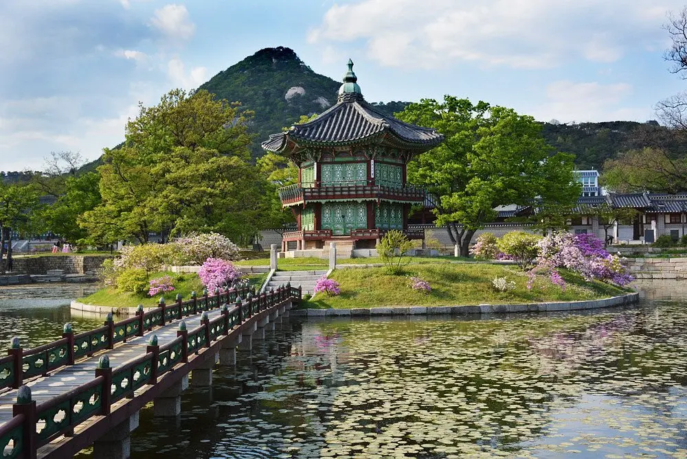 The Hexagonal Pavilion sits in a pond surrounded by trees and flowers at Gyeongbokgung Palace in Seoul, South Korea.