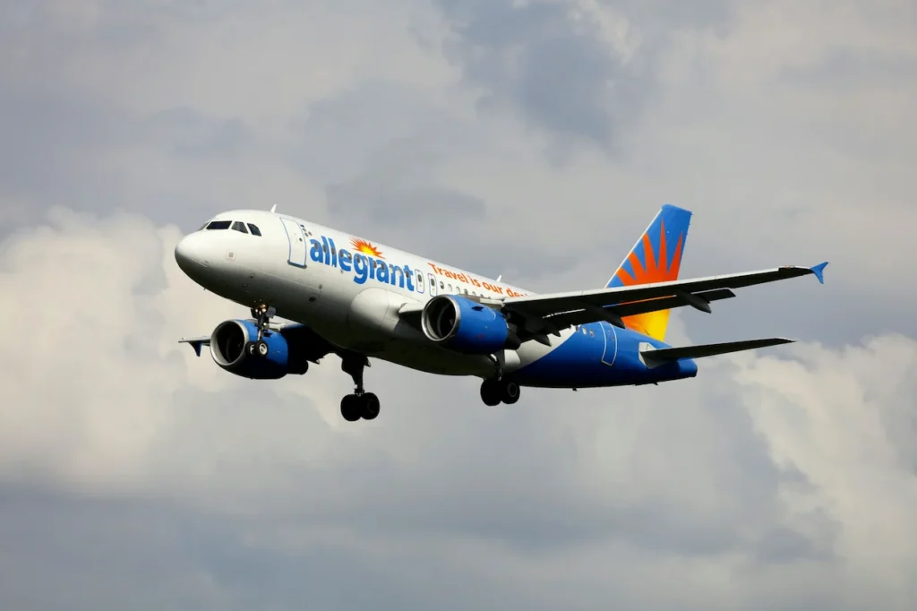 Allegiant Air Airbus jet with gear down ascending against grey clouds