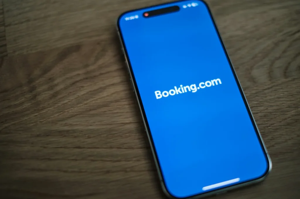 iPhone screen displaying the white Booking.com logo over a bright blue background on a wooden surface