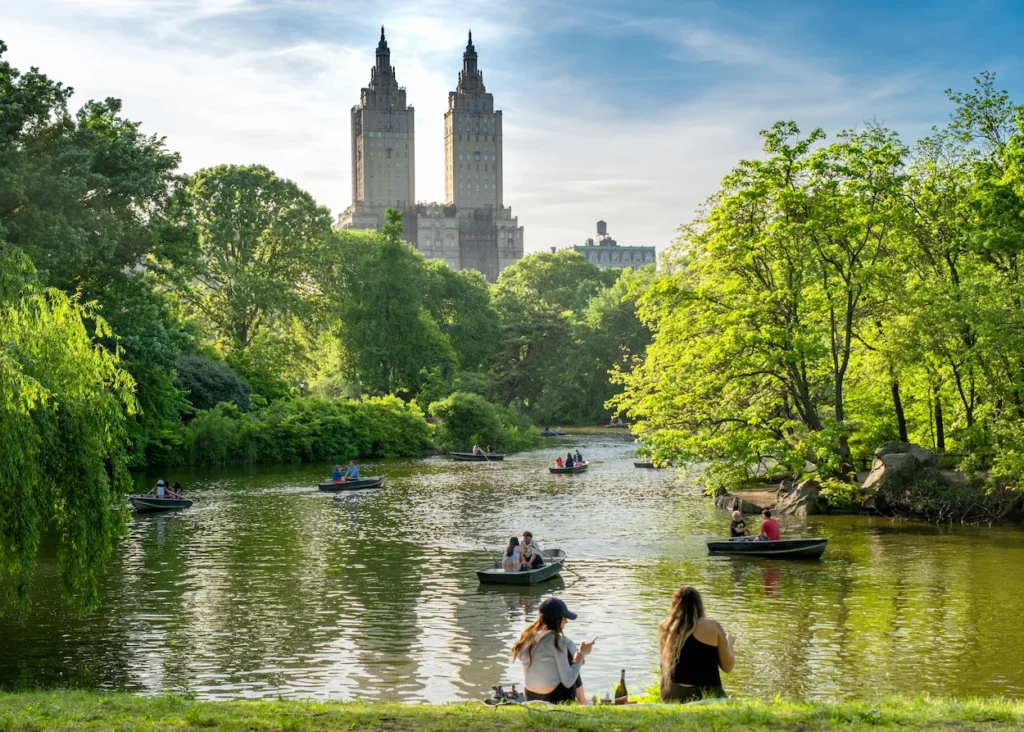 Central Park Lake filled with rowboats against a backdrop of lush green trees and the San Remo apartment towers