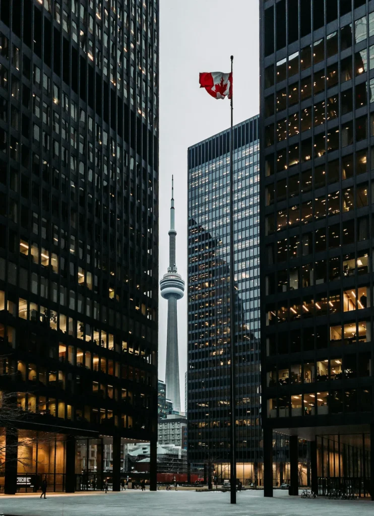 CN Tower and waving Canadian flag framed between black skyscraper office towers in Toronto