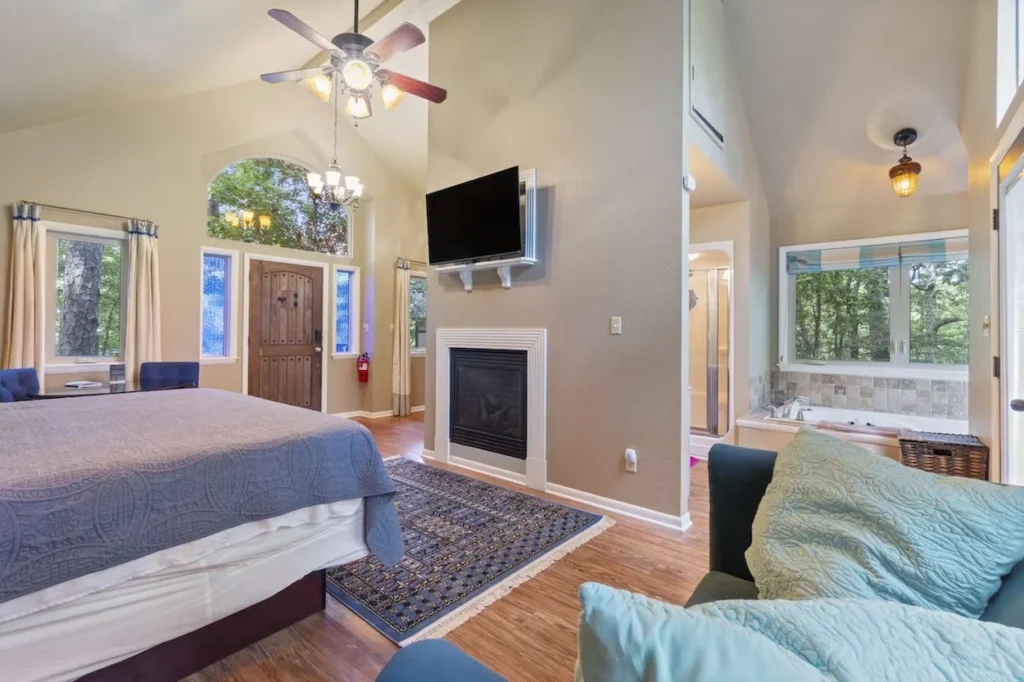 A cabin bedroom with a fireplace, wall-mounted television, and an indoor jacuzzi tub