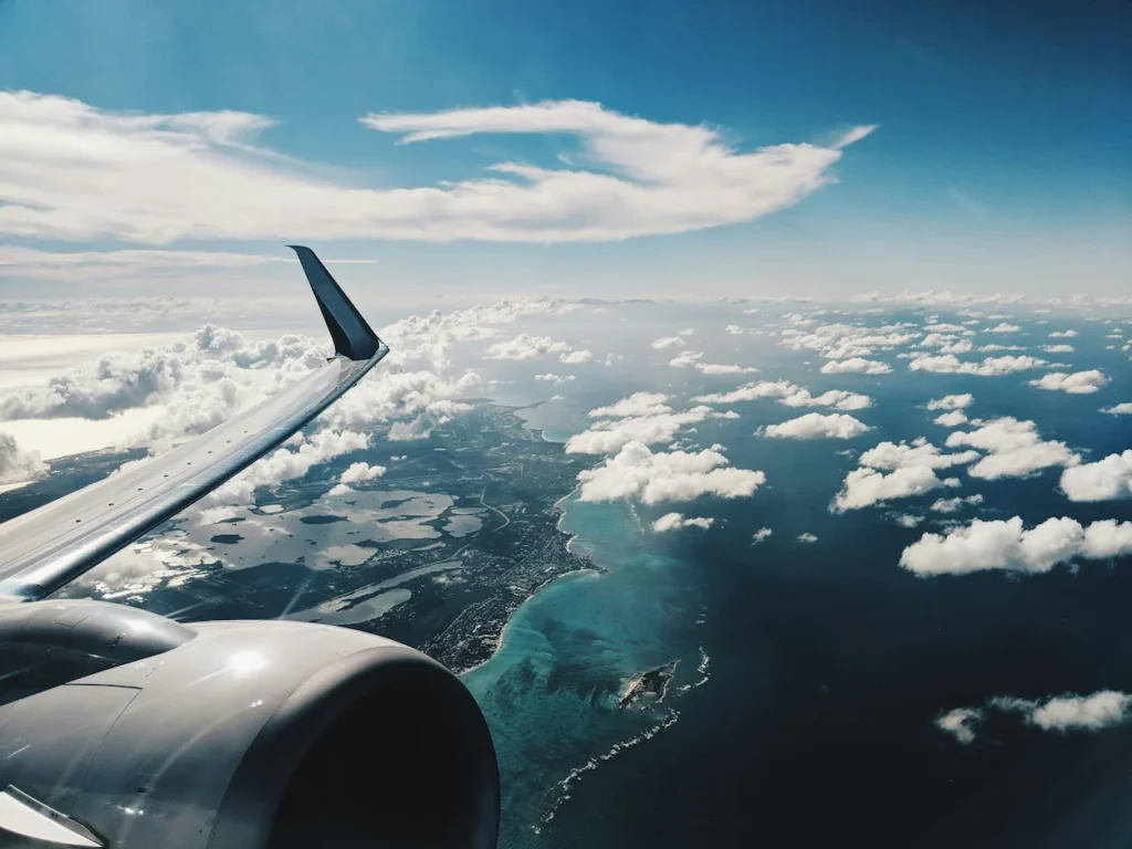 Airplane wing and engine over turquoise Caribbean coastal waters and clouds