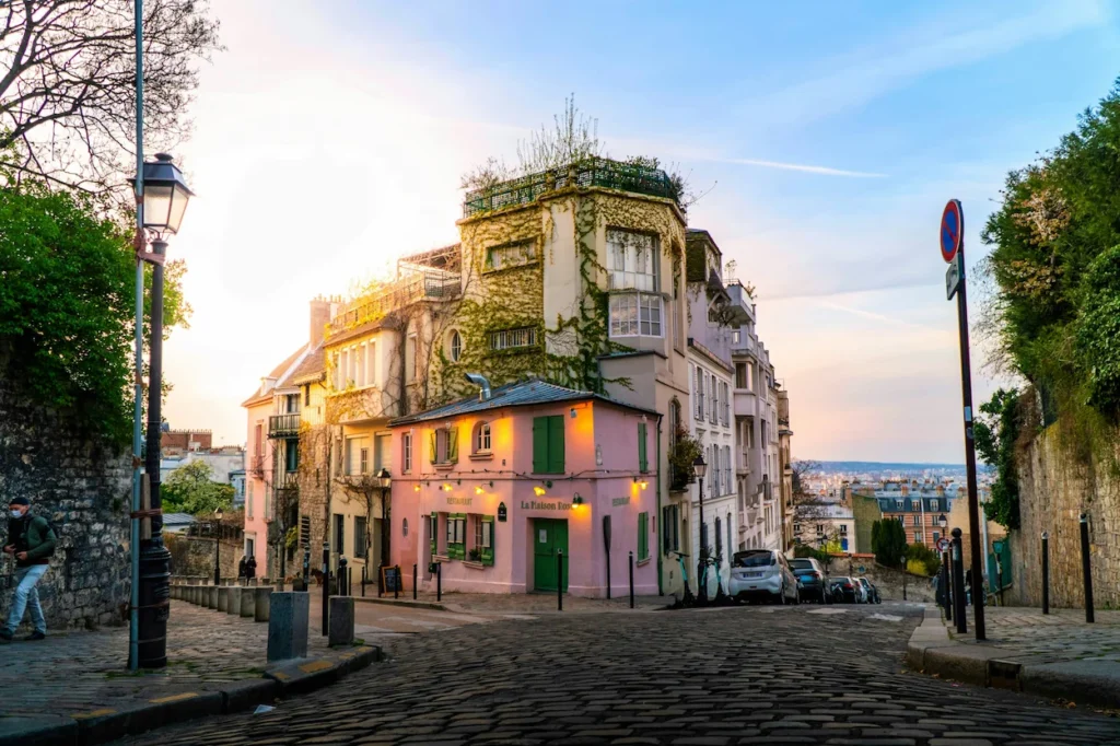 The iconic La Maison Rose cafe on a sloped cobblestone street corner in the Montmartre district of Paris during golden hour