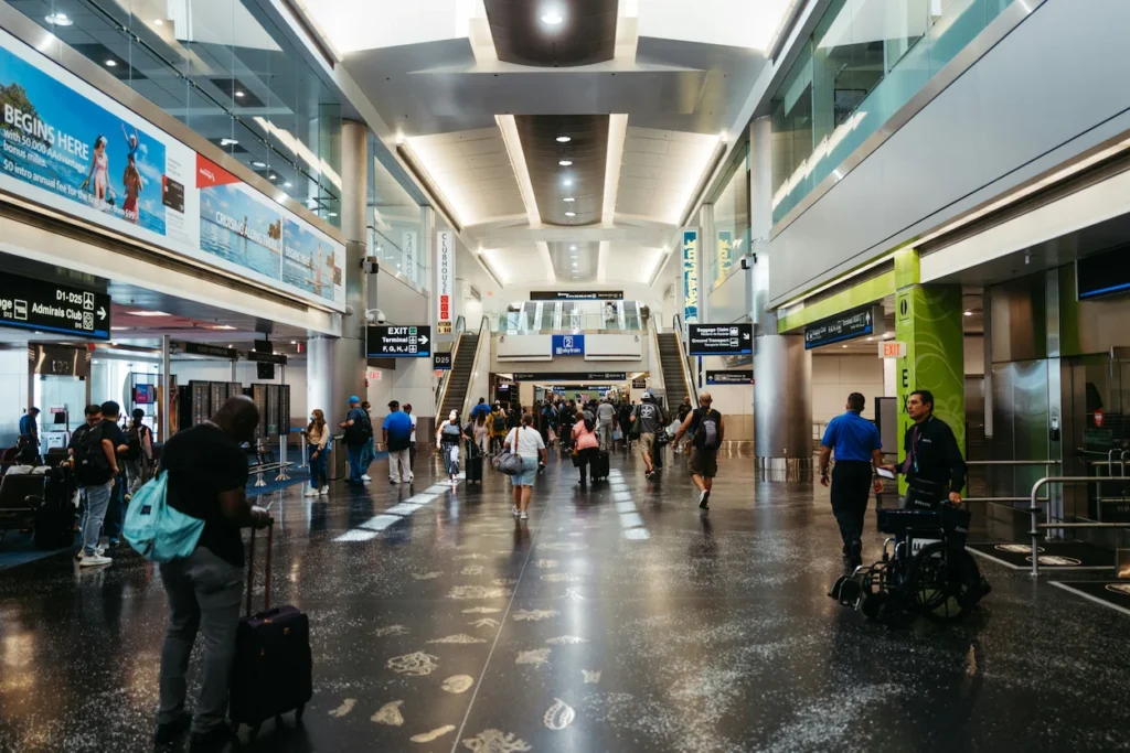 Travelers walking with luggage down a wide Miami airport concourse with dark terrazzo flooring
