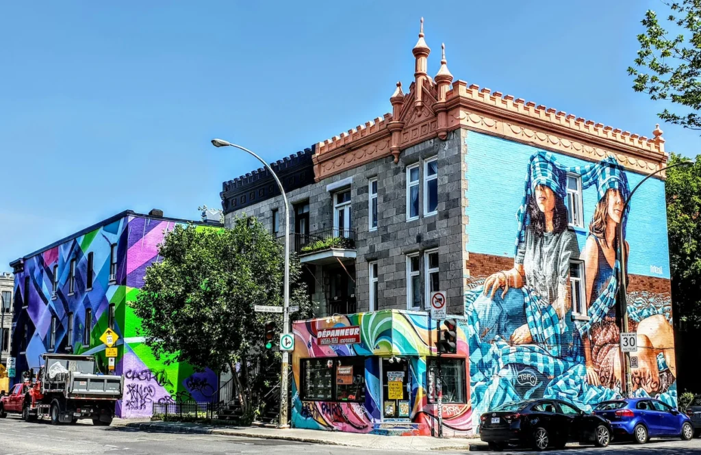 Montreal street corner with colorful building murals and a local dépanneur shop under a bright blue sky