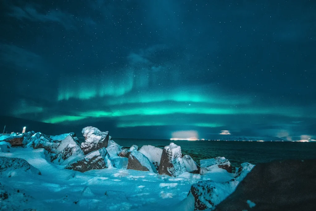 Green aurora borealis glowing over a snow-covered rocky coastline at night