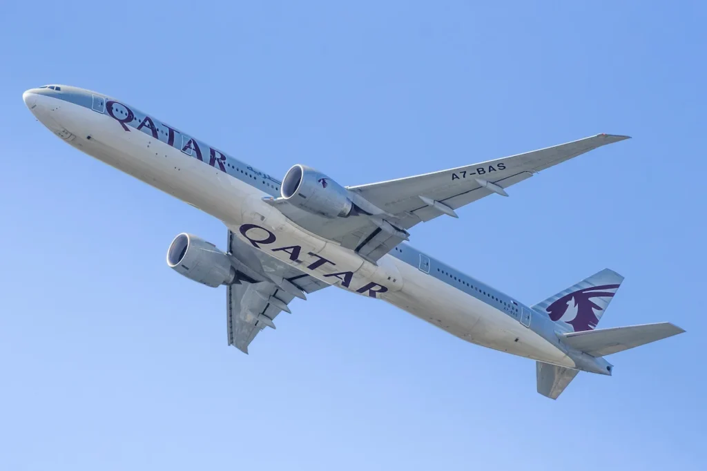 Qatar Airways Boeing 777 passenger jet soaring through a clear blue sky after takeoff