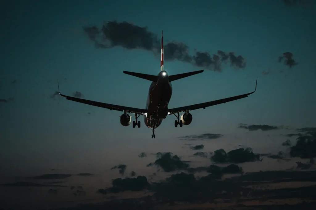 Swiss Air passenger plane silhouetted at dusk with landing gear down and a glowing white logo on the red tail