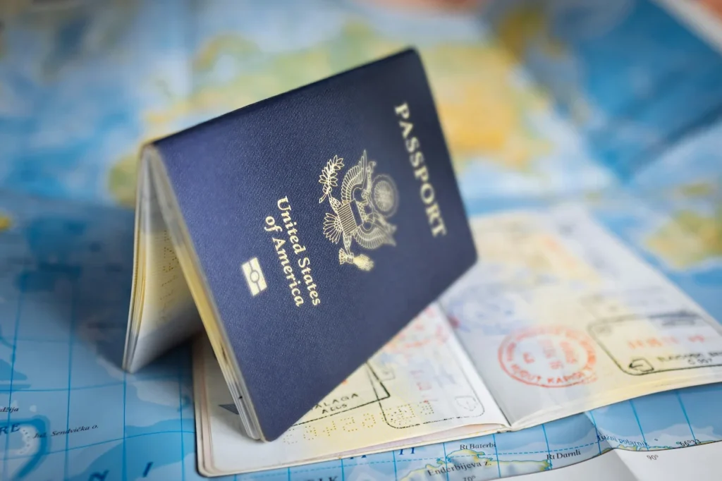 A blue United States passport resting open on a world travel map with visa stamps