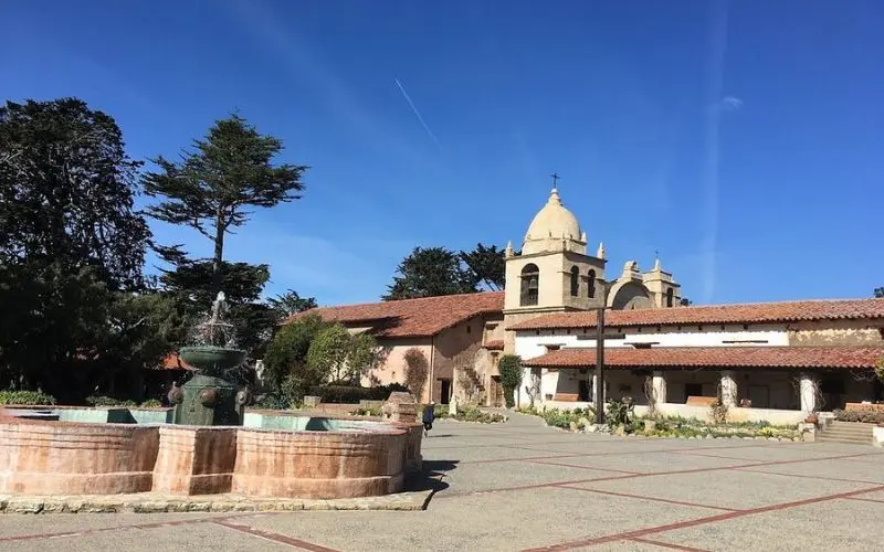 The courtyard and fountain at Carmel Mission under a clear blue sky.