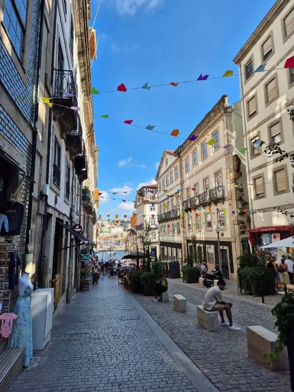 Colorful flags hang above the cobbled street of Ribeira on a sunny day.