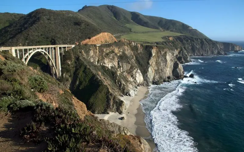 Scenic coastal view of Bixby Creek Bridge over cliffs by the ocean.