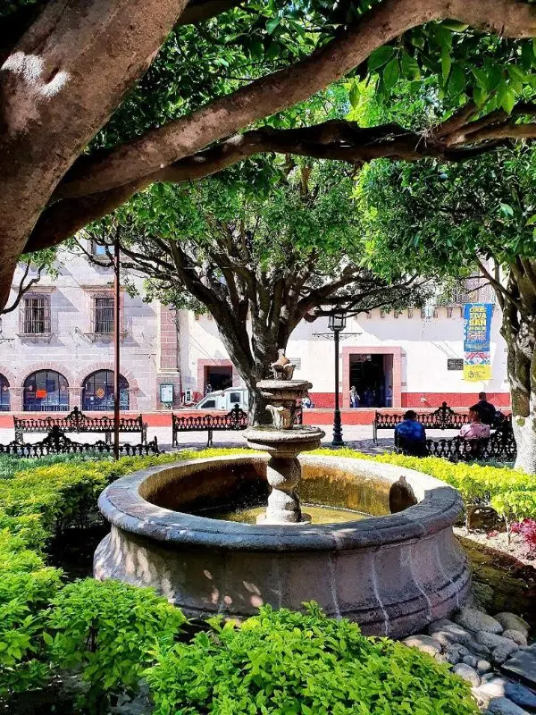 A stone fountain sits in a shaded plaza in San Miguel de Allende.