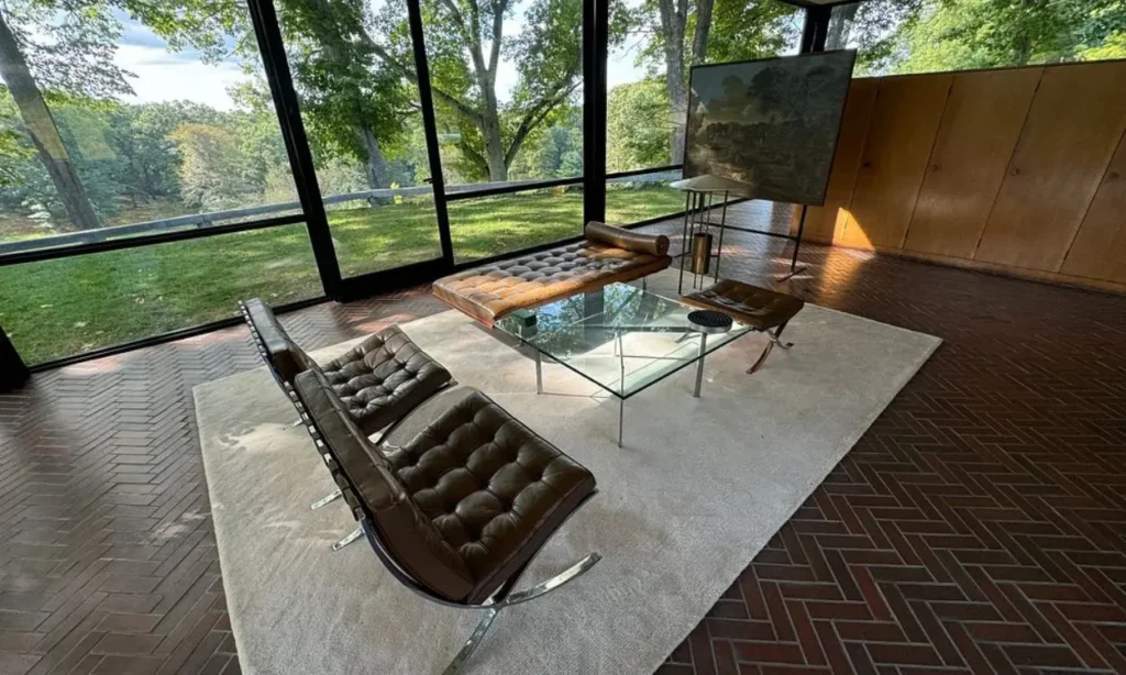 Modern interior with leather chairs, glass table, and large windows overlooking trees at The Glass House.
