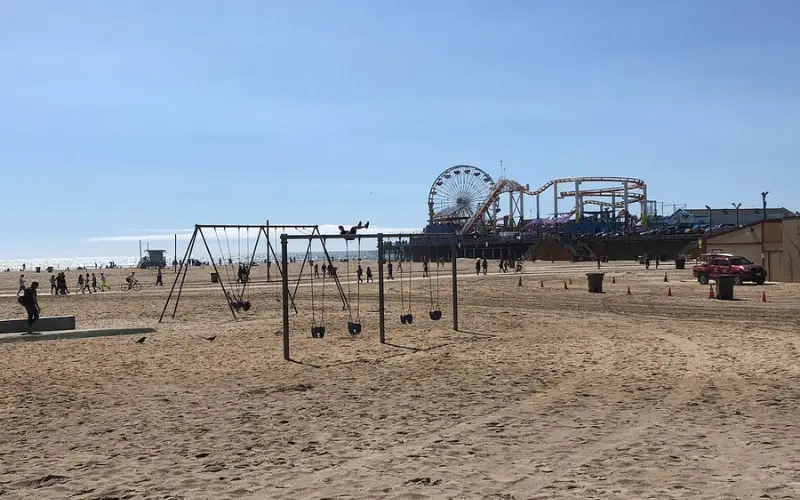 Outdoor gym and swings with Santa Monica Pier rides in the background at Muscle Beach.