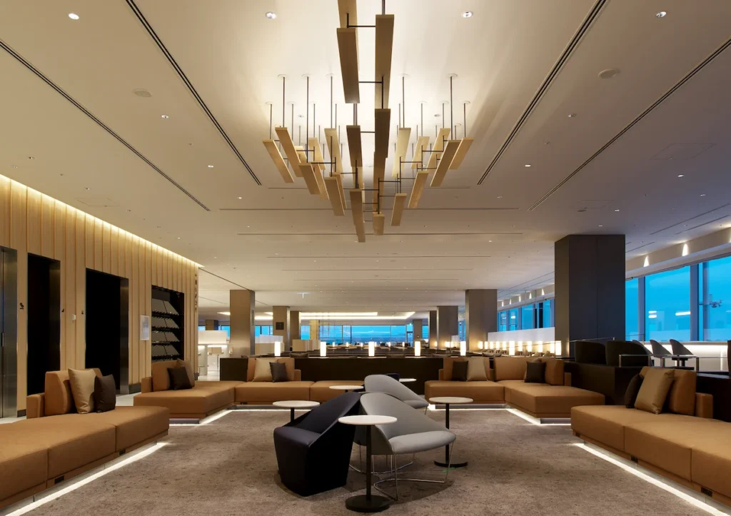ANA Suite Lounge seating area with brown sofas, modern armchairs, and a large wooden stick chandelier