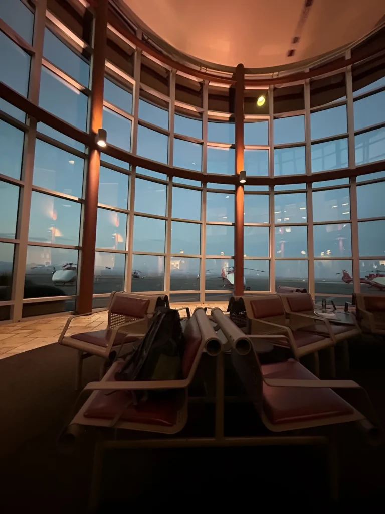 Interior lounge at Boulder City Municipal Airport with curved grid glass walls overlooking a tarmac with red and white helicopters