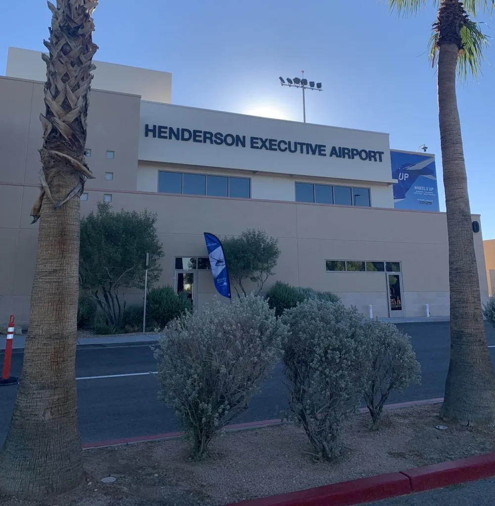 Exterior view of the Henderson Executive Airport terminal building framed by palm trees and desert shrubs under a bright sky