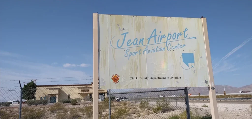 Weathered outdoor sign for Jean Airport Sport Aviation Center in Nevada behind a chain-link fence